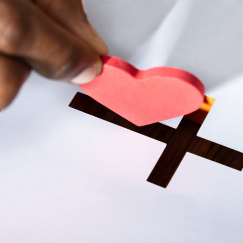 Close-up Of A Man's Hand Inserting Red Heart Shape In Crucifix Slot